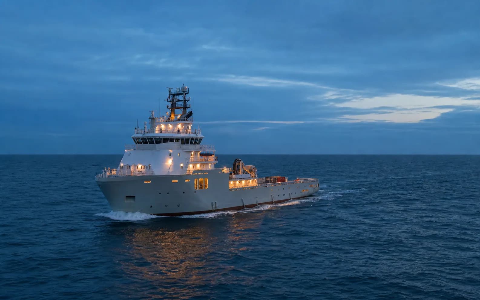 An offshore support vessel underway on open water at blue hour.